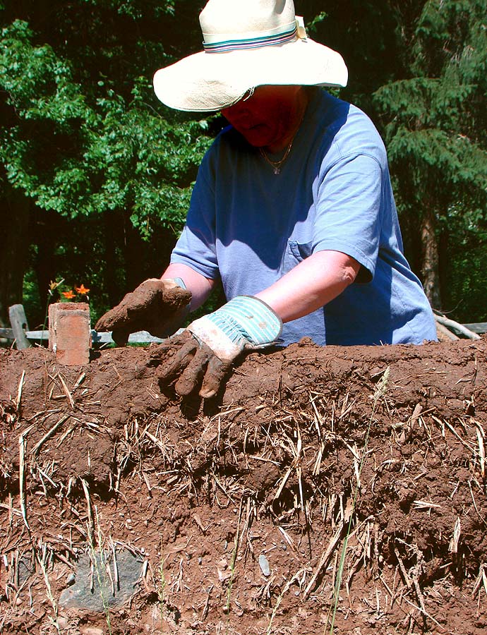 Frau beim manuellen Bau einer Cob-Wand mit Lehmerde, Sand und Stroh.