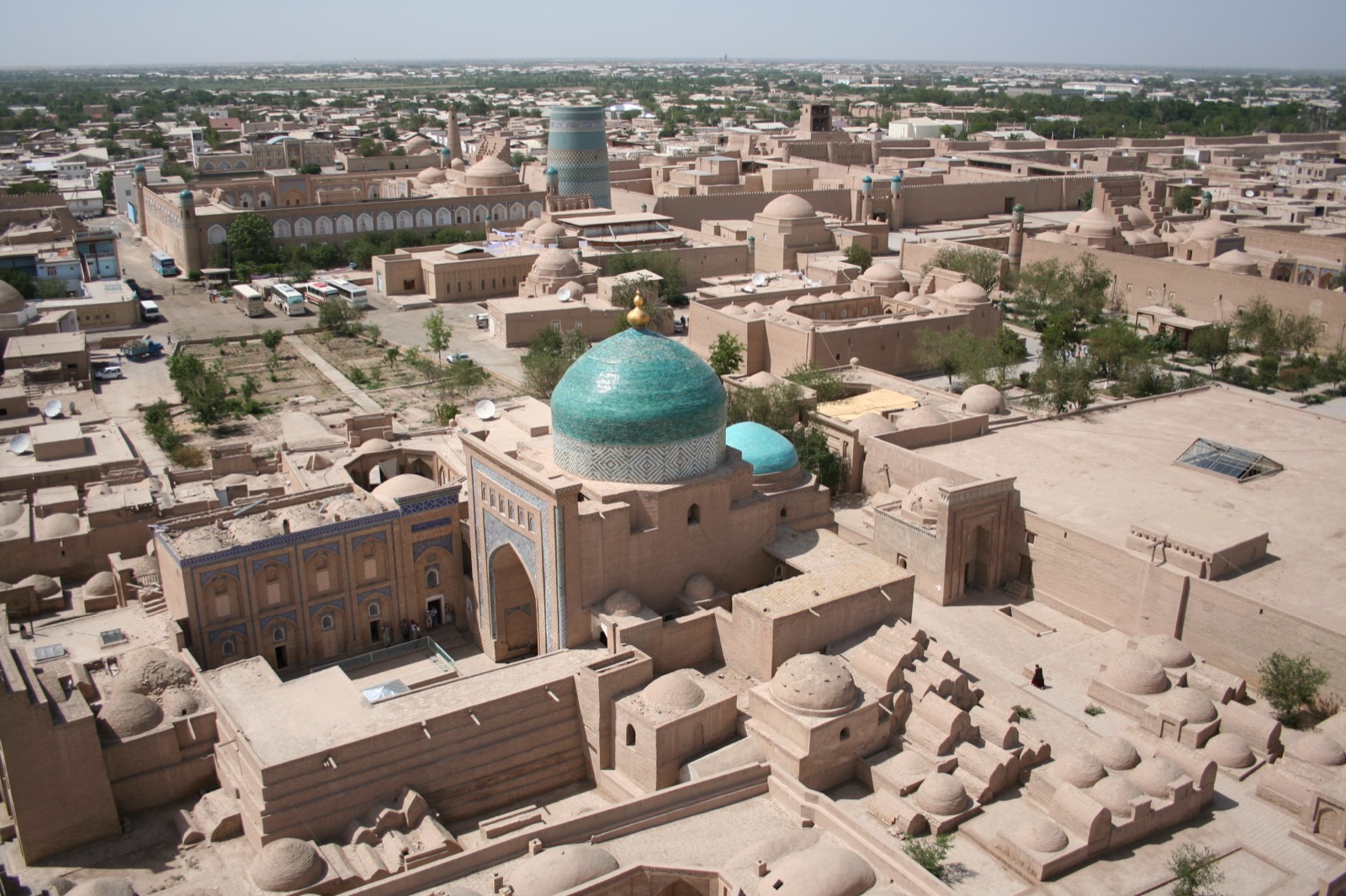 Blick vom Islam-Khodja-Minarett über die ummauerte Altstadt Itchan Kala in Chiwa: dicht gedraengte Lehmziegelbauten, erdfarbene Kuppeln, Mausoleen und Medresen mit tuerkisfarben gekachelten Kuppeln, umgeben von den massiven Lehmmauern der Stadt.