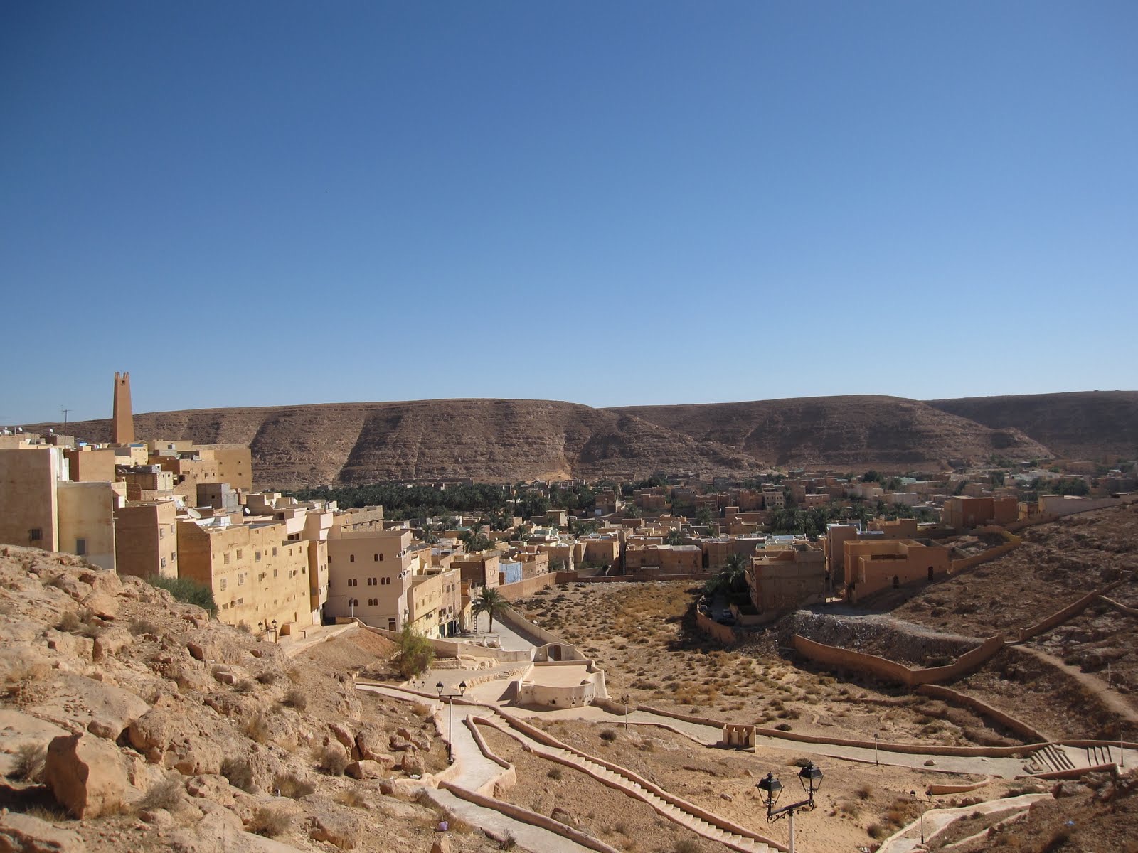 Blick auf die traditionelle Lehmbau-Siedlung El-Atteuf im M'Zab-Tal bei Ghardaïa, Algerien: dicht gestaffelte ockerfarbene Lehmhäuser mit Minarett vor der Saharahochebene.